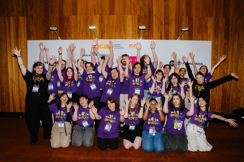 Group of people in purple shirts celebrating with raised arms in a wooden-paneled venue.