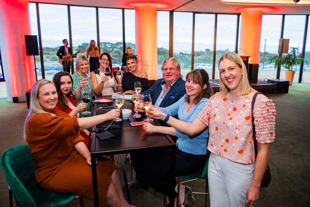 Group toasting with drinks at a casual gathering in modern office space with city views.