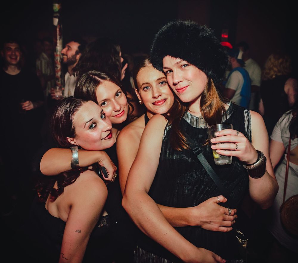 Group of friends having fun and taking selfies together at a dimly lit nightclub or party venue.