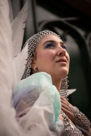 A person wearing chainmail headpiece and ethereal  fantasy costume poses dramatically.