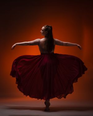 Dramatic silhouette of a dancer in a flowing red dress against a dark background.