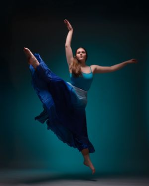 Ballet dancer in a blue dress performs graceful movements against a teal backdrop.