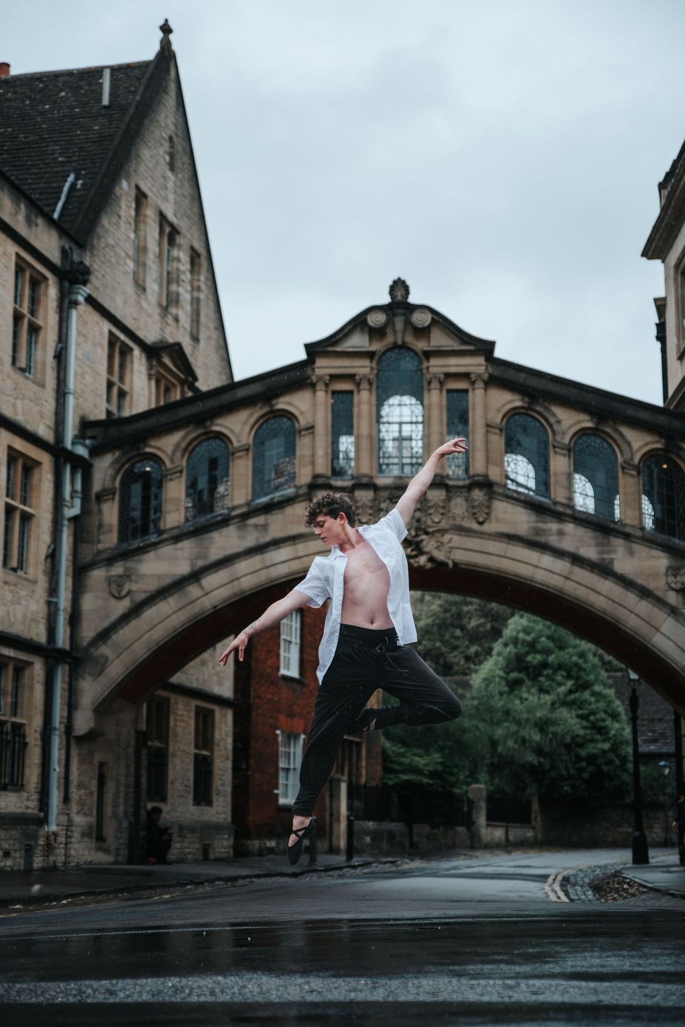 Dancer performing a graceful leap under a historic stone bridge arch.