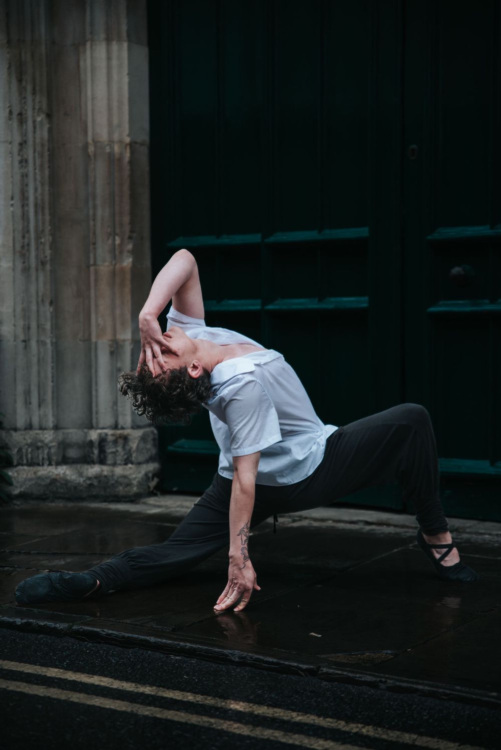 Dramatic dance pose captured against architectural elements in low light.
