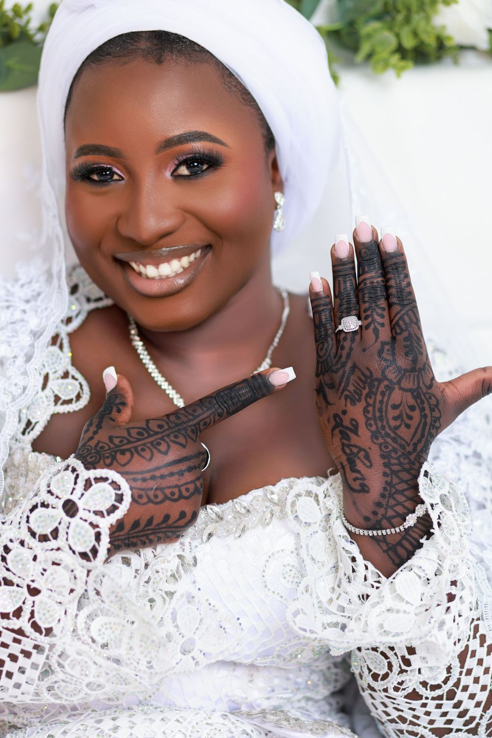 Bridal portrait showcasing intricate henna designs on hands and elegant white lace attire.