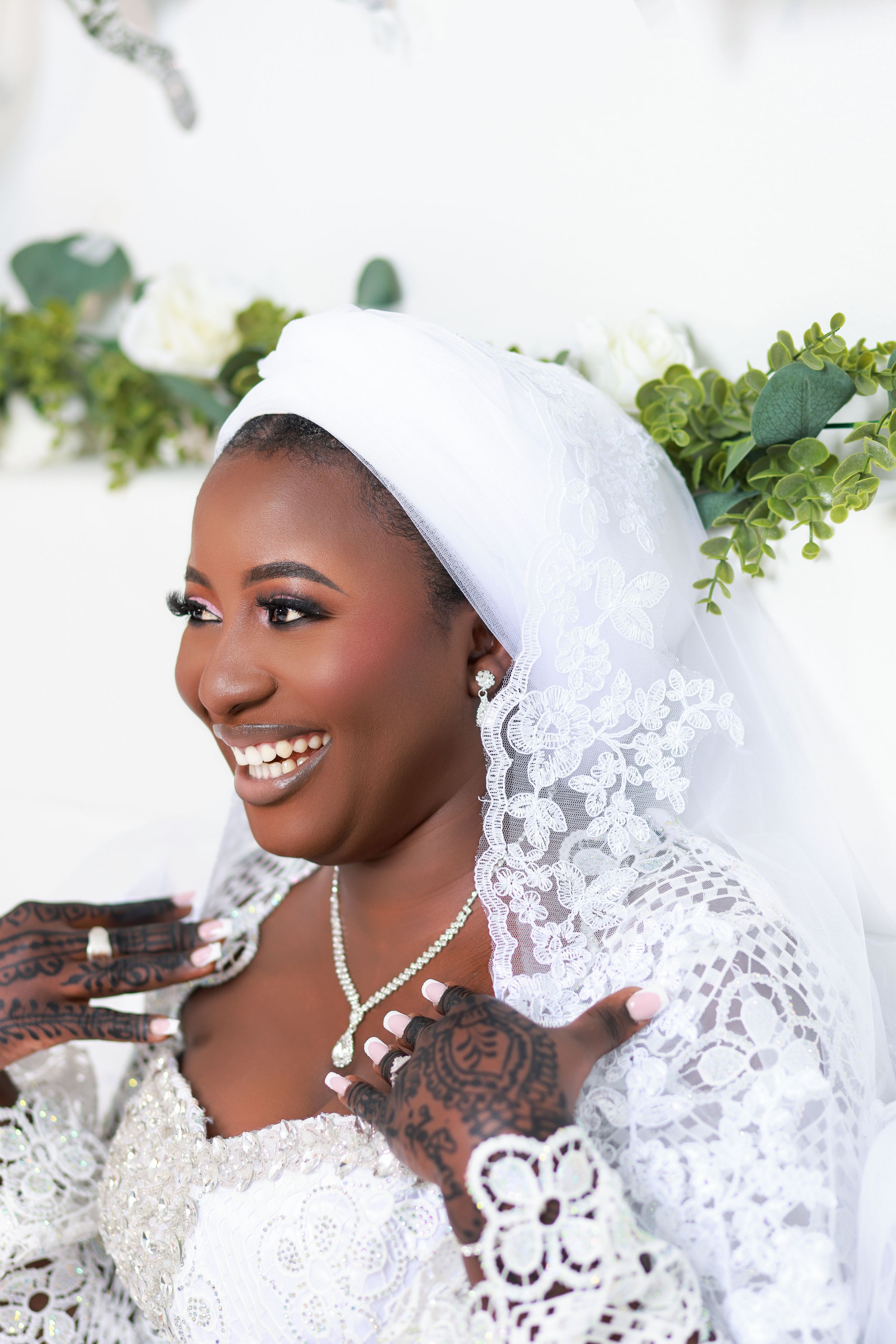 Elegant bridal portrait featuring white lace dress and headpiece with green foliage accents.