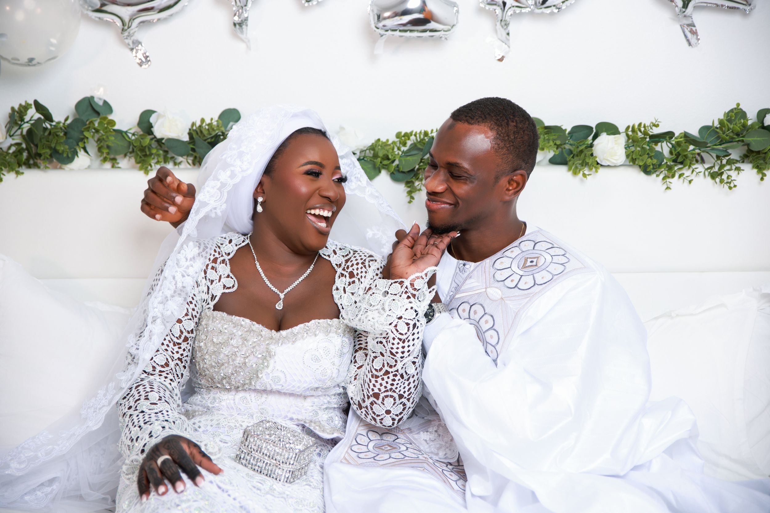 Newlyweds share candid laughter during photo shoot with silver balloon decorations.