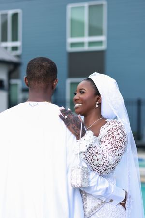 Newlyweds share intimate moments during outdoor photo session against blue building.