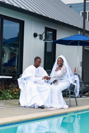 Bride and groom in elegant white attire share joyful moment beside swimming pool.