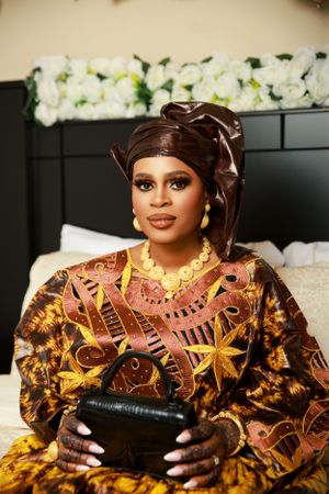 Traditional African fashion shoot featuring vibrant gold and brown patterned dress against floral backdrop.