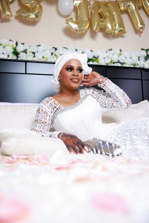Bridal portrait in white lace dress laying on rose petal covered bedding.
