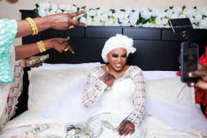 Person in white lace dress poses during wedding celebration with floral backdrop.