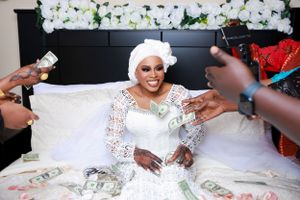 Wedding celebration scene with person in white dress handling dollar bills on decorated bed.