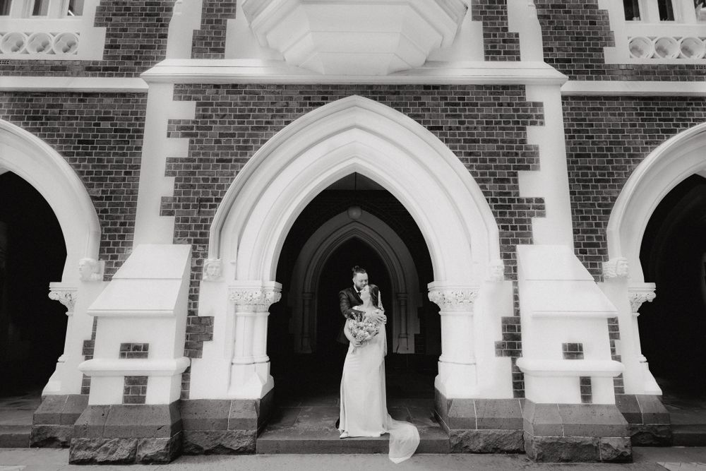 Elegant black and white photograph of a couple in a historic brick building, captured by Apertured Media Auckland Wedding Photographer.