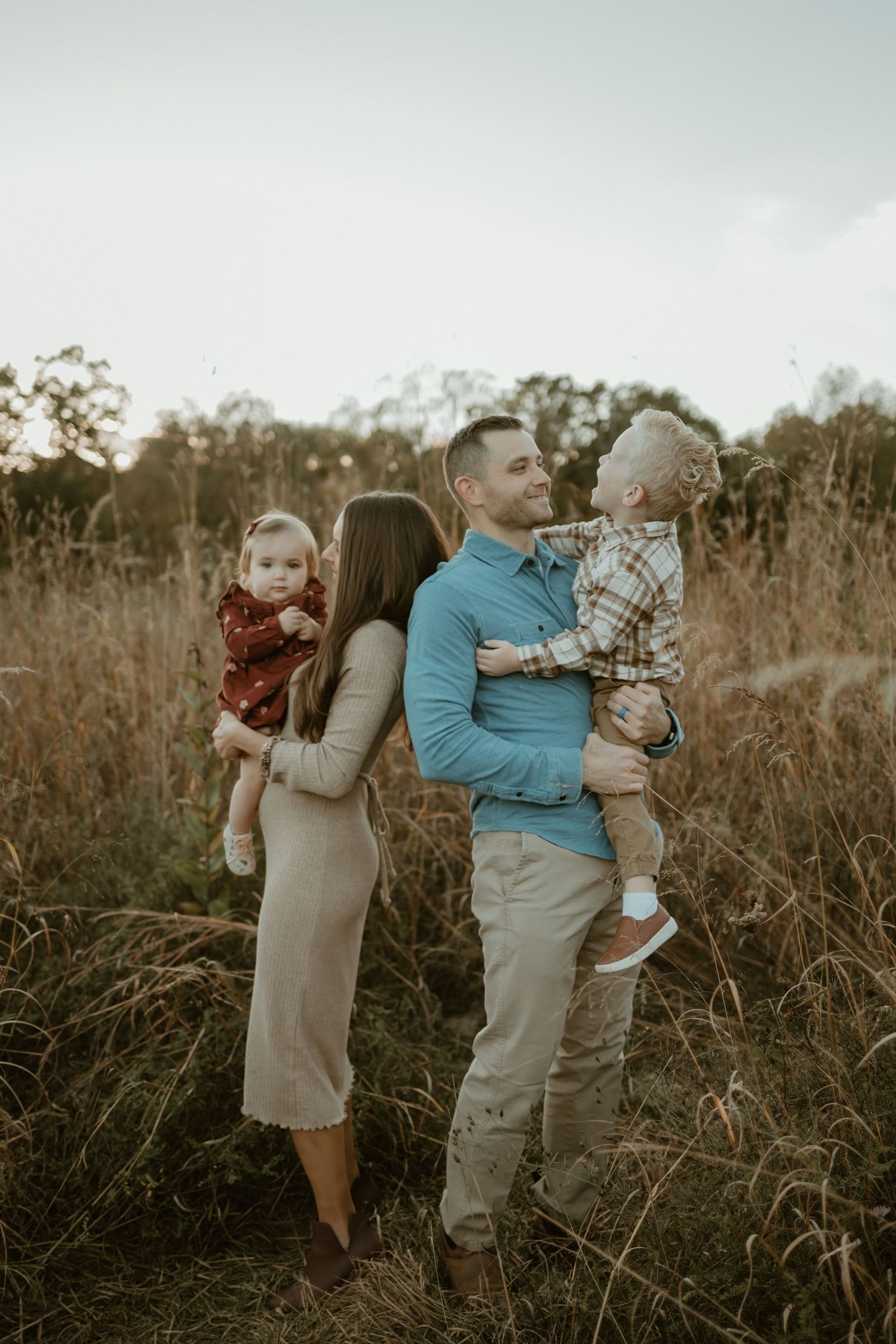 A family sits together on a blanket in an orchard at sunset with orange and rust-colored tones.