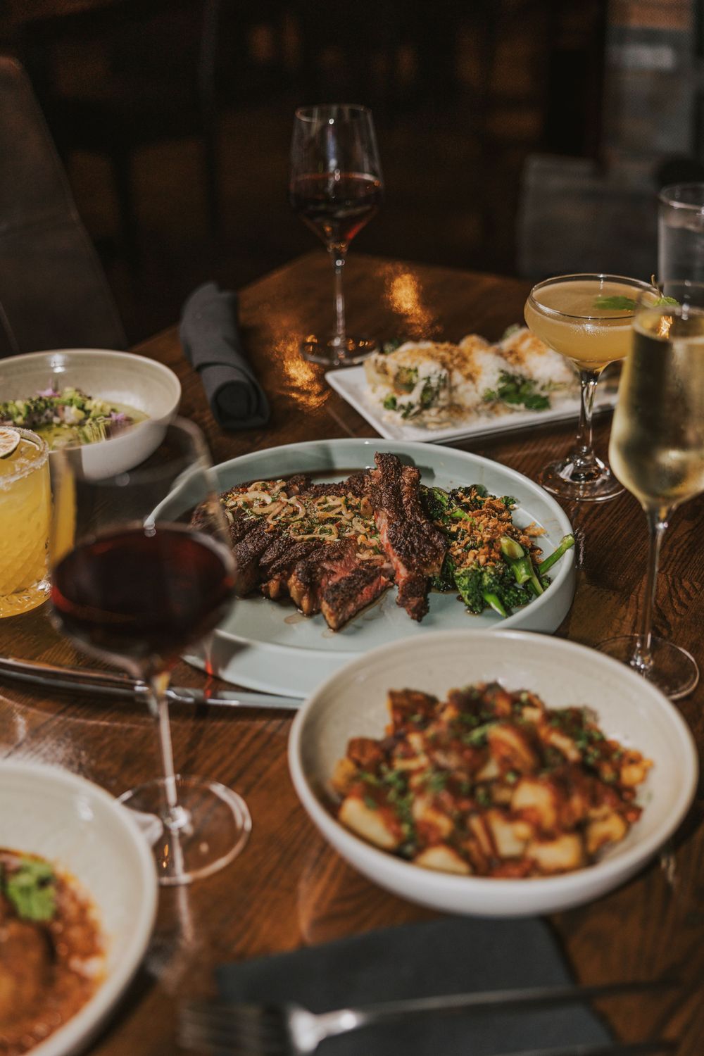 Fine dining table setting with grilled meat, pasta dishes and cocktails.