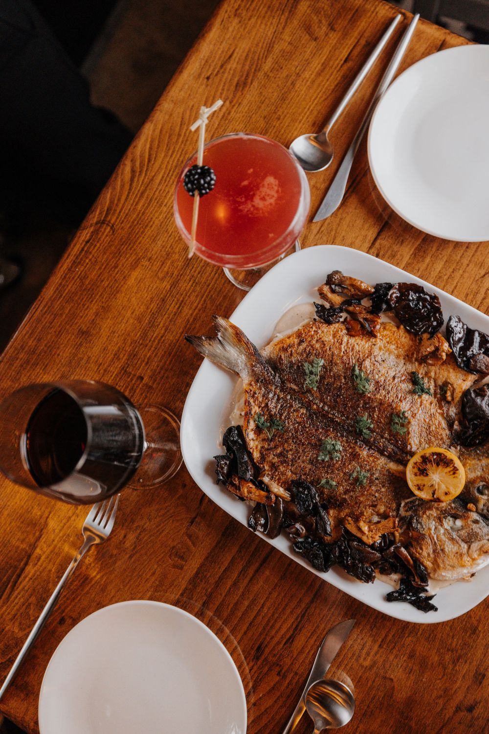 Roasted meat dish with red cocktail and wine glass on wooden table.