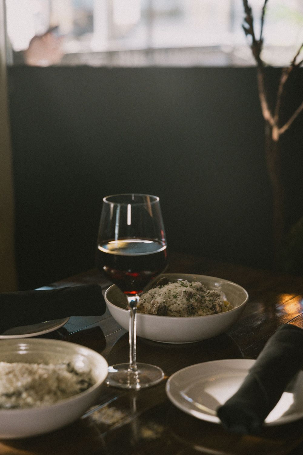 A glass of red wine beside bowls of herbed rice on a dark wooden restaurant table in moody lighting.