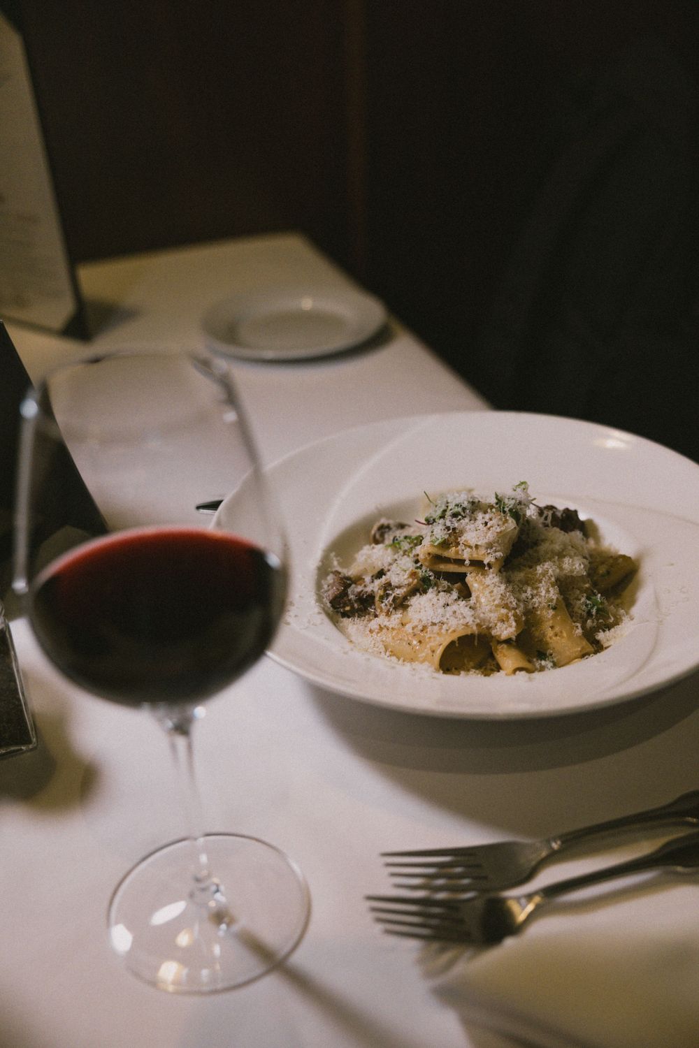 Pasta dish with parmesan cheese served alongside red wine on white tablecloth.