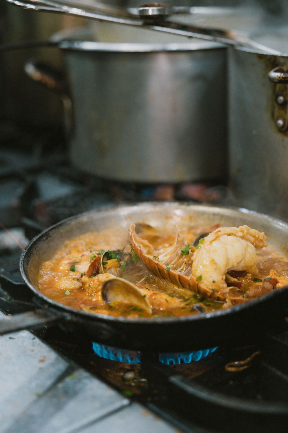 Seafood stew simmering in pan over blue gas flame.