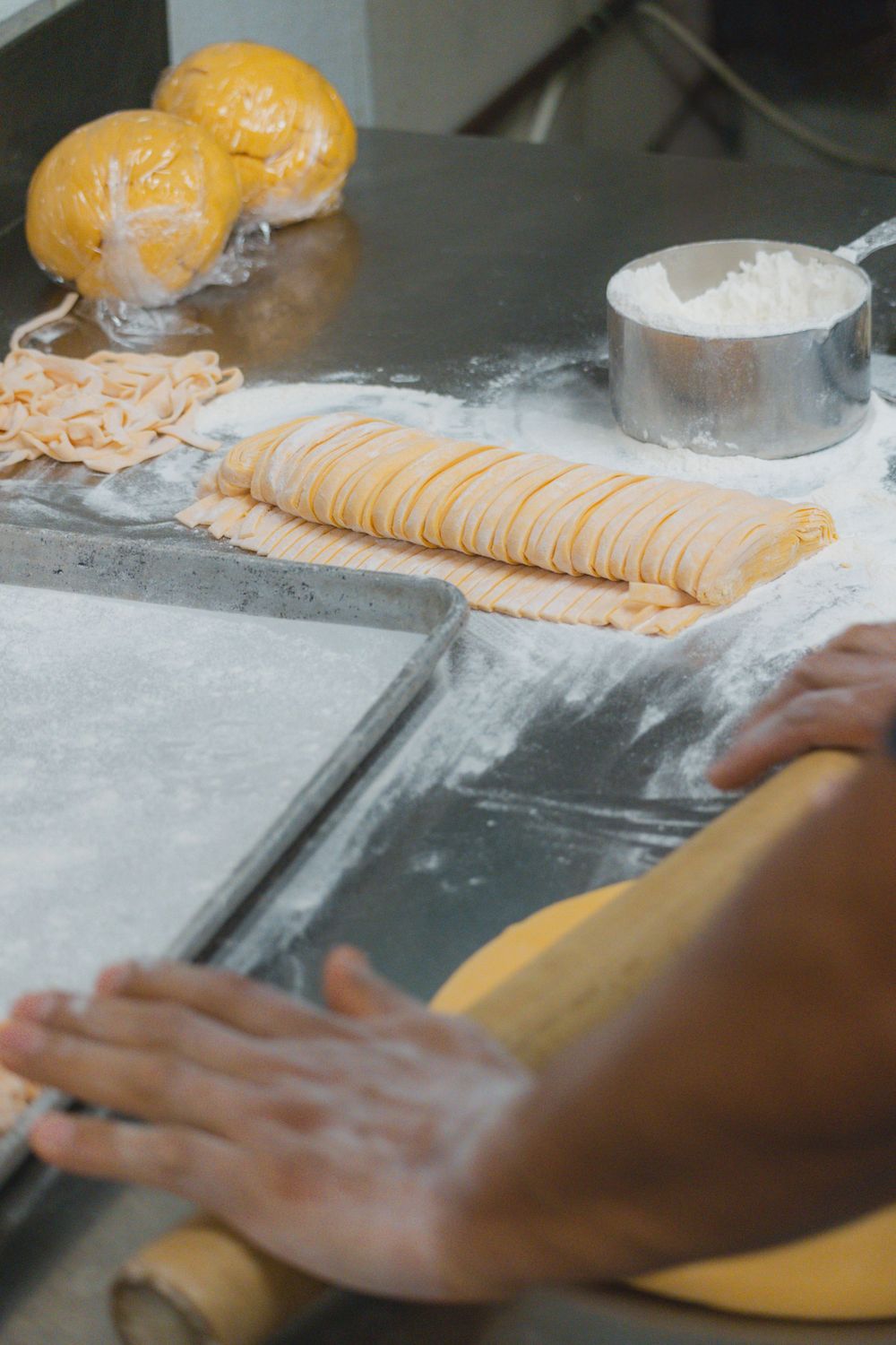 Hands rolling out fresh pasta dough on a floured surface in a kitchen.