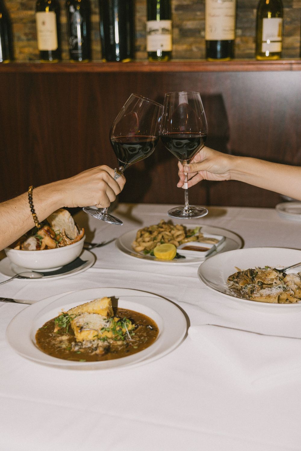 Fine dining table with wine toast over gourmet dishes on white tablecloth.