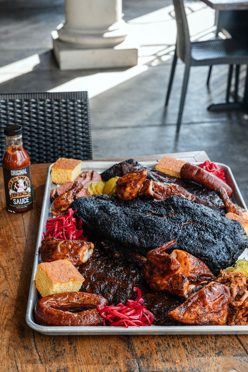 A large BBQ platter with smoked brisket, ribs, sausage, cornbread, and coleslaw served on a metal tray with BBQ sauce.
