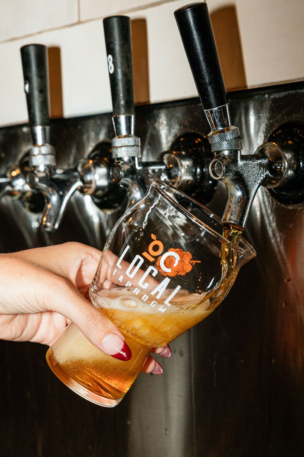 Hand holding an OC Local Taproom branded glass being filled with craft beer from stainless steel draft taps.
