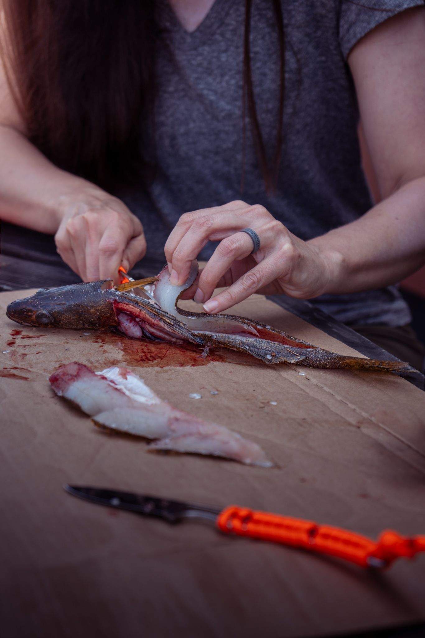 Close-up view of hands filleting fresh fish on a wooden cutting board with orange tool visible.