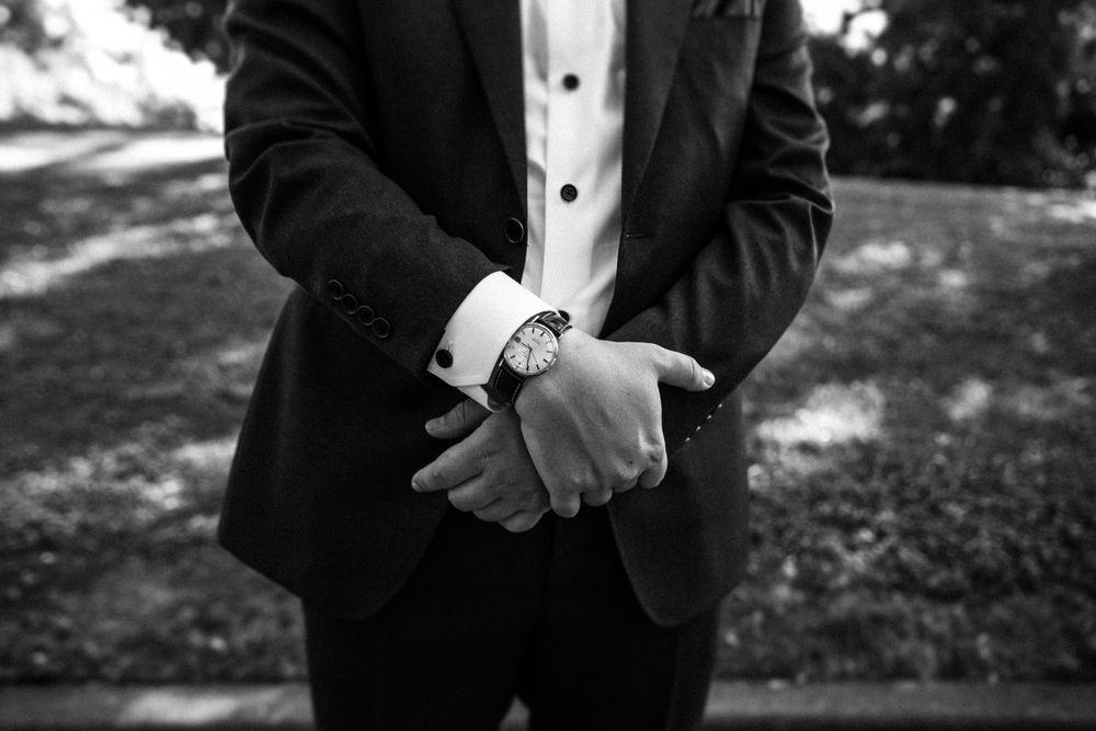 Black and white detail shot of groom adjusting watch while wearing formal tuxedo.