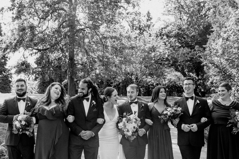 Wedding party in black and gray formal attire poses together on an outdoor pathway.