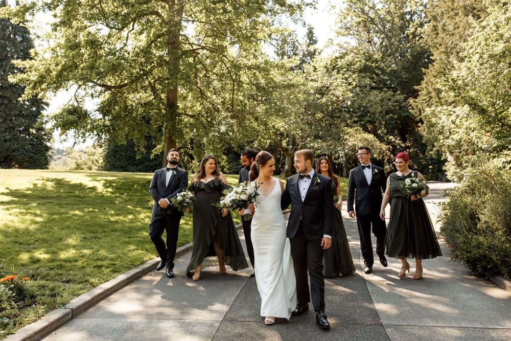 Wedding party walking and laughing together on outdoor garden path during sunny celebration.