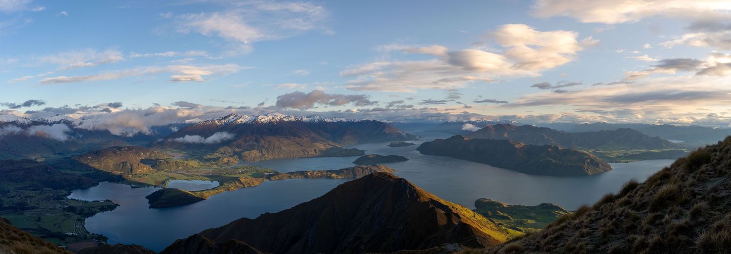 Panoramic view of lakes and mountains under a dramatic cloudy sky at sunset.