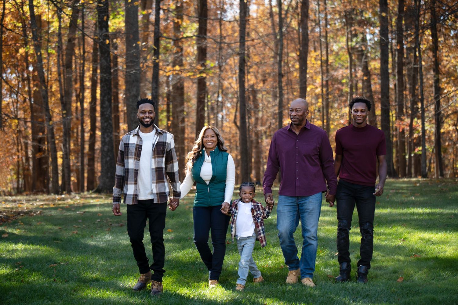 Group walking together on grass path through autumn woods with orange and yellow fall foliage.