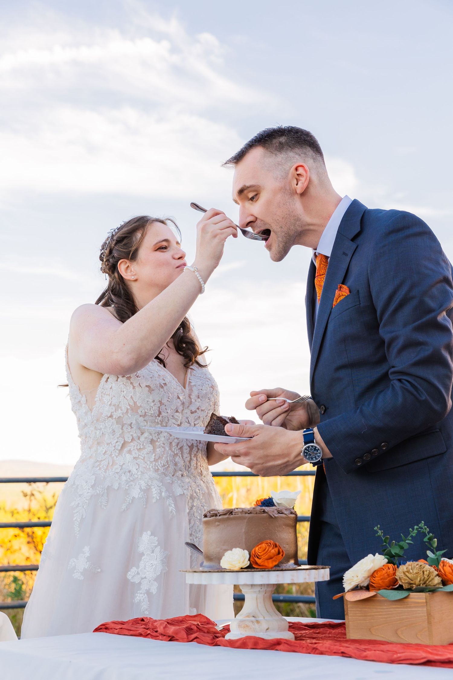 Newlyweds share a playful moment while tasting their wedding cake at an outdoor reception.