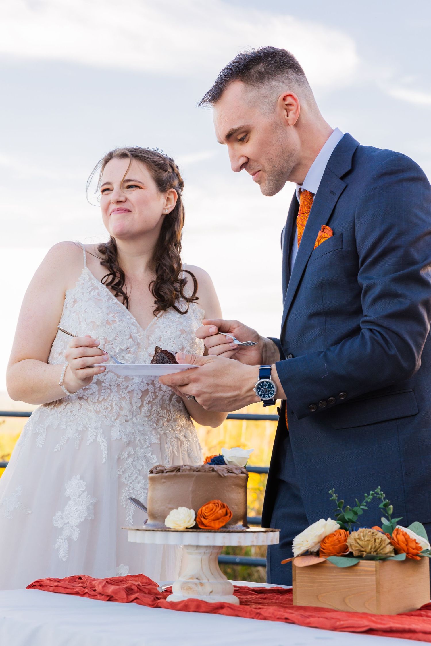 Couple enjoying their wedding cake during an outdoor autumn celebration.