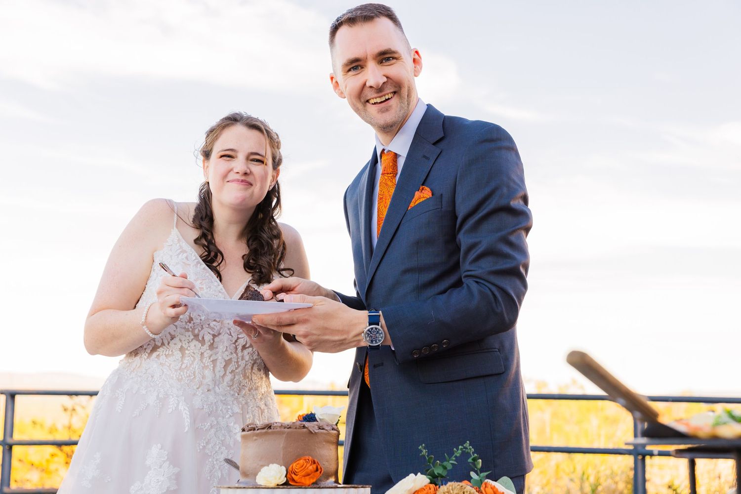 Wedding couple smiling while sharing cake at their outdoor reception.