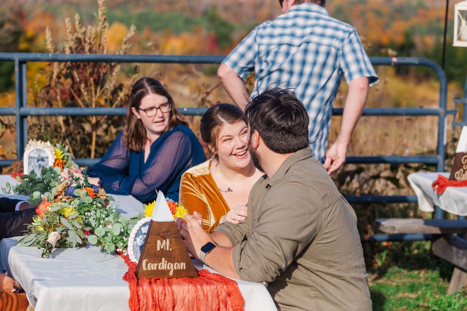 Casual outdoor wedding reception with guests sitting at decorated table.