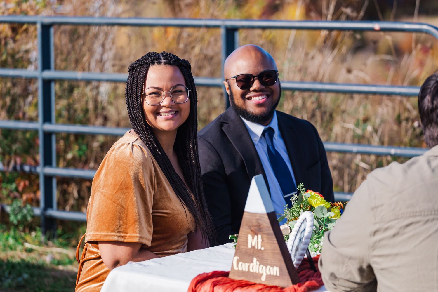 Wedding guests enjoy outdoor reception with autumn foliage in background.
