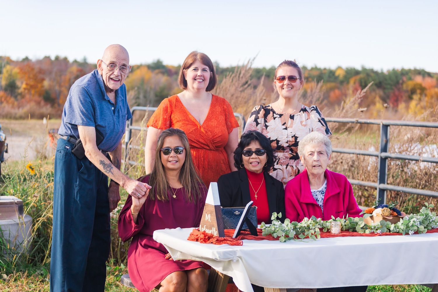 Group gathers around decorated table at outdoor autumn wedding reception.