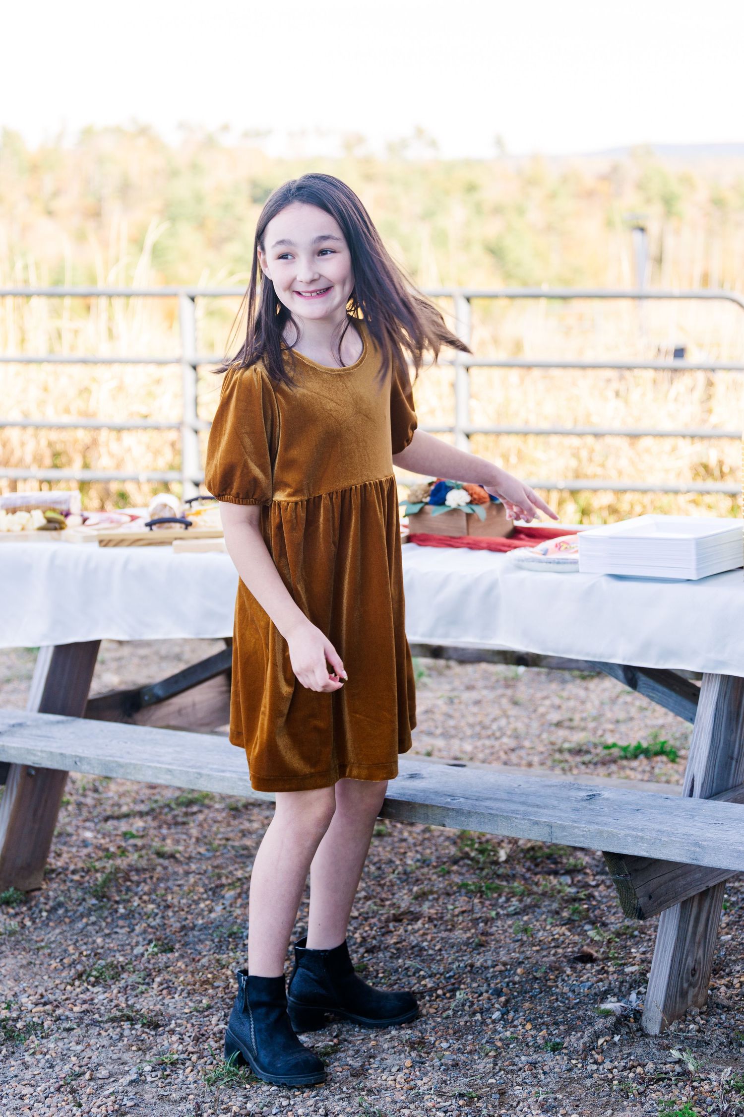 Brown velvet dress and boots outfit against autumn backdrop with picnic table and natural scenery.