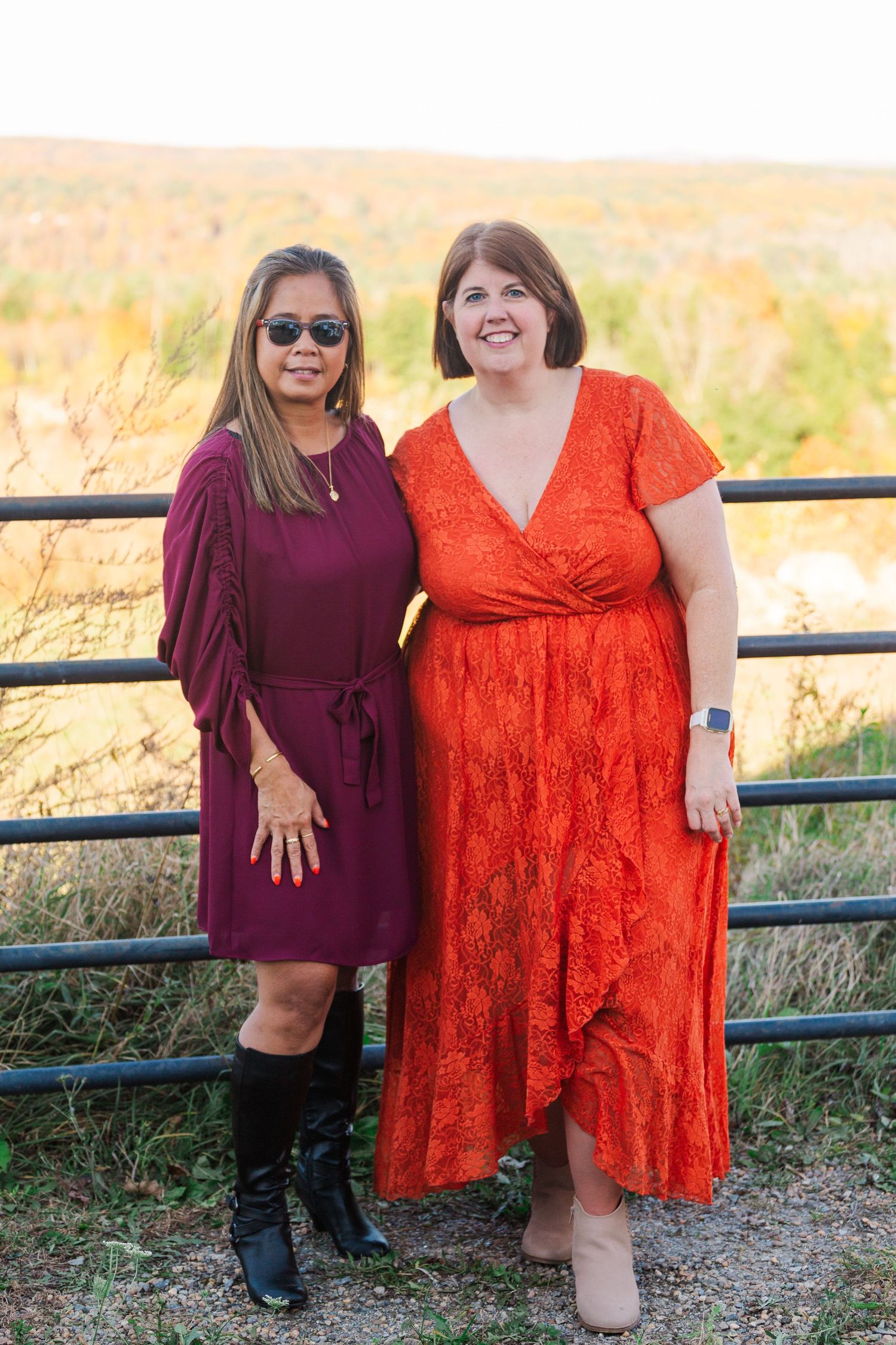 Two friends in burgundy and orange dresses pose together at outdoor event.