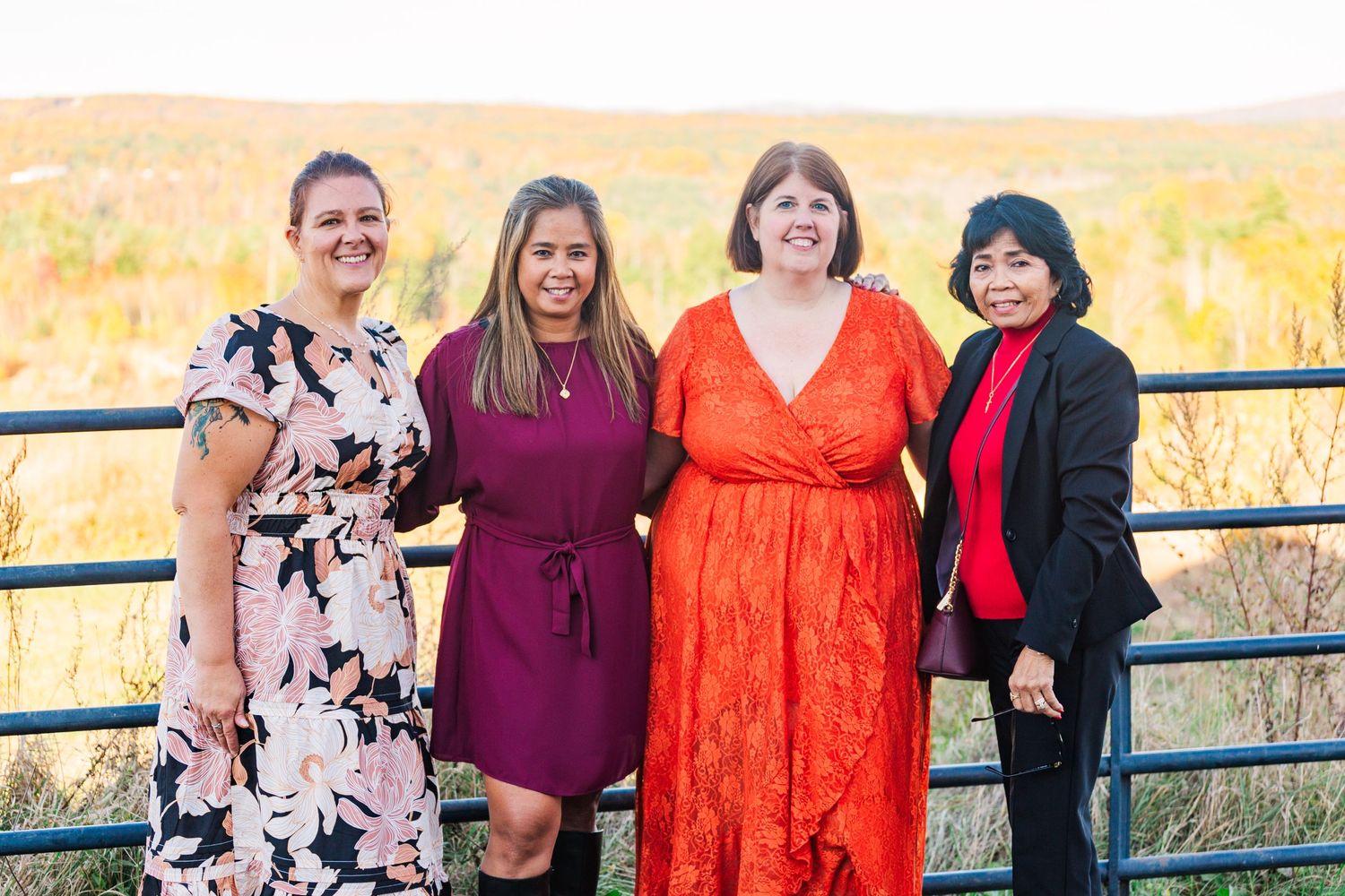 Group of friends in colorful dresses gathered at outdoor celebration with autumn scenery.