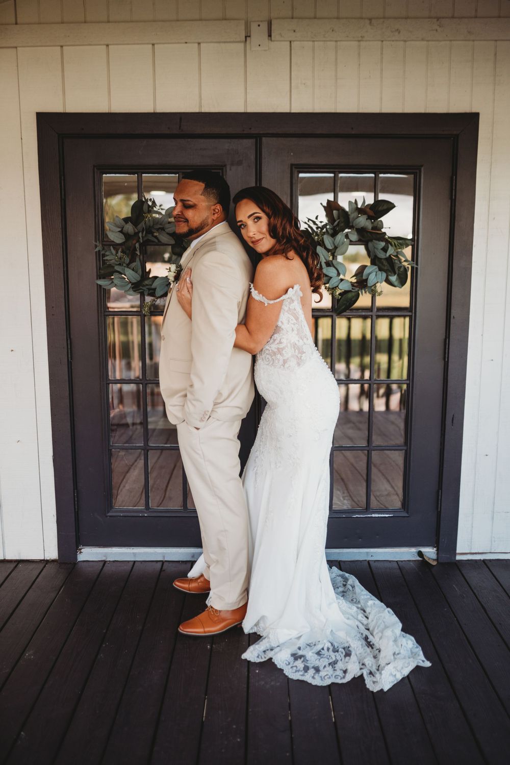 A couple in wedding attire poses against a dark doorframe on a wooden porch.