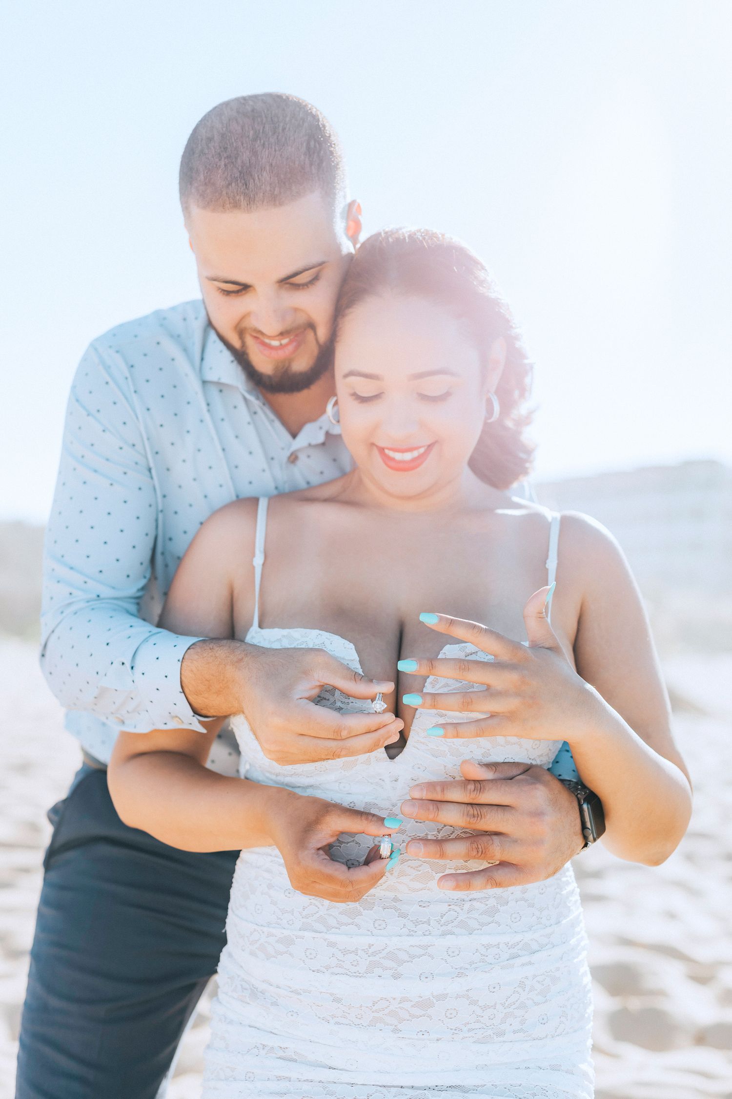 Romantic beach engagement photos showing a couple looking at their rings together.