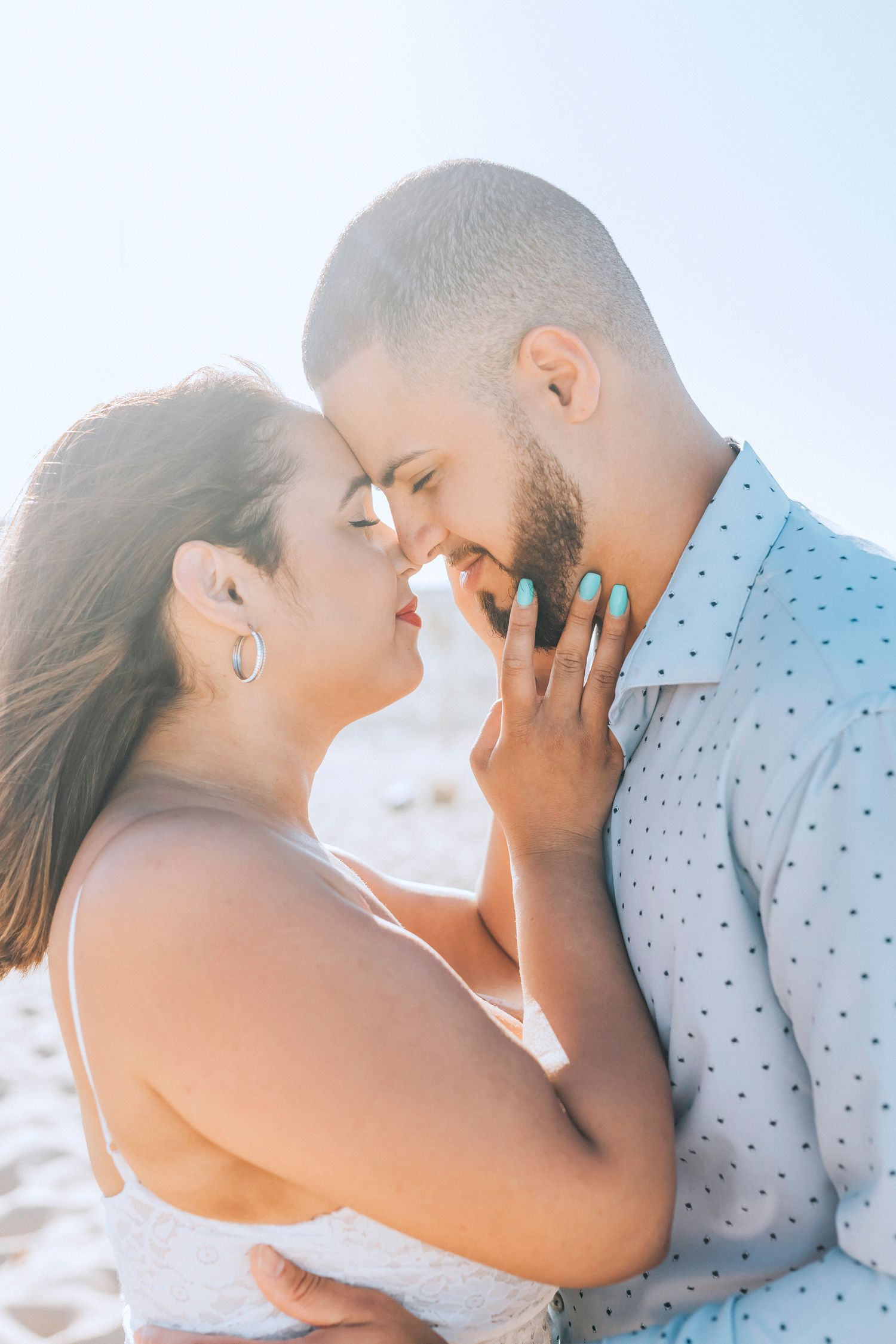 Intimate beach engagement portraits with soft sunlight and tender moments.