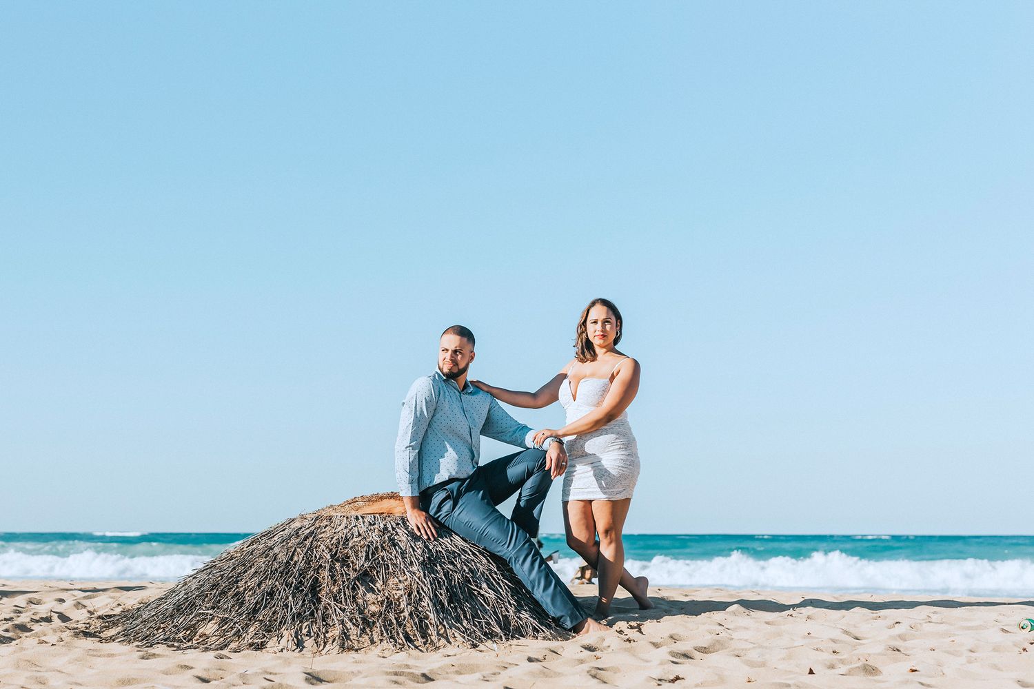 Couple posing playfully on a sandy beach with ocean waves in the background.
