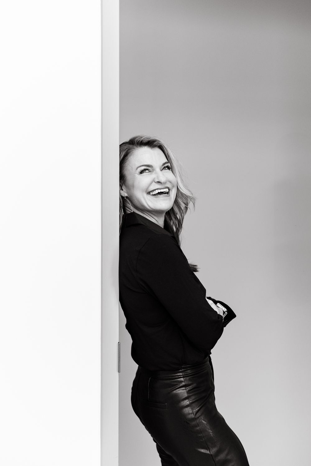 Black and white studio portrait of a person in black clothing laughing joyfully against a light background.