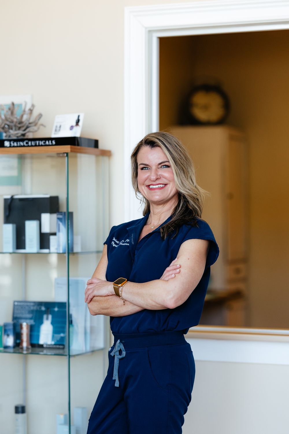 Medical professional in navy scrubs stands confidently with crossed arms near product shelving.