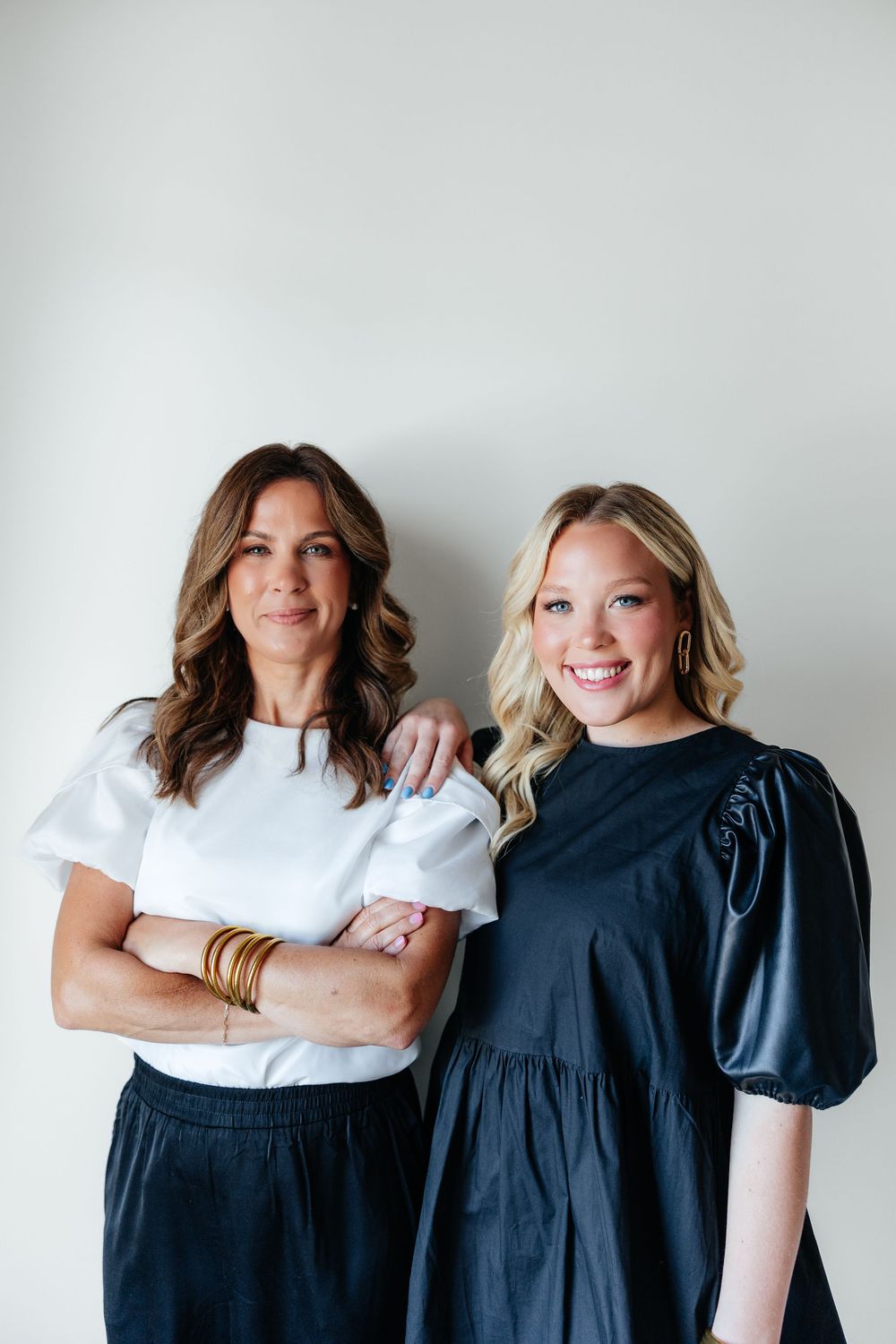 Two people wearing contrasting white and black dresses pose together against a light background in a series of photos.